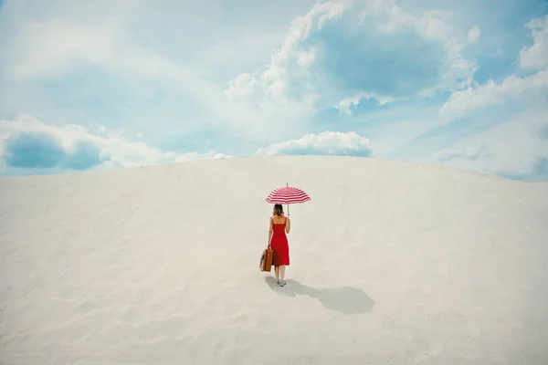 Abito rosso con ombrellone e valigia in spiaggia — Foto Stock