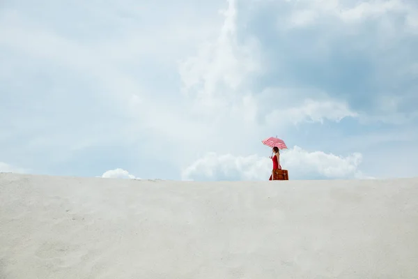 Röd klänning med paraply och resväska på stranden — Stockfoto