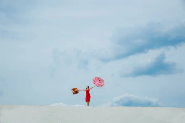 Röd klänning med paraply och resväska på stranden — Stockfoto