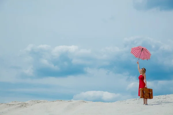 Czerwona sukienka z parasolem i walizka na plaży — Zdjęcie stockowe