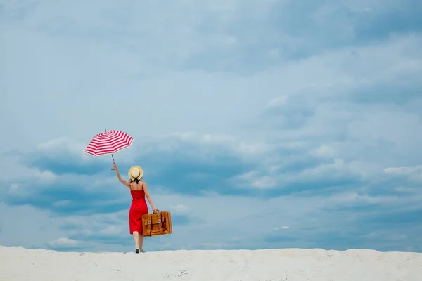Rode jurk met paraplu en koffer op het strand — Stockfoto