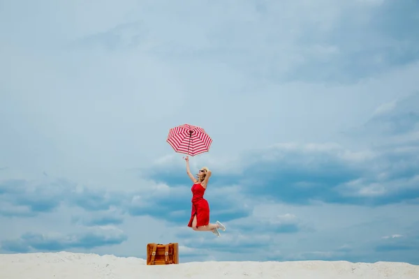 Rode jurk met paraplu en koffer op het strand — Stockfoto