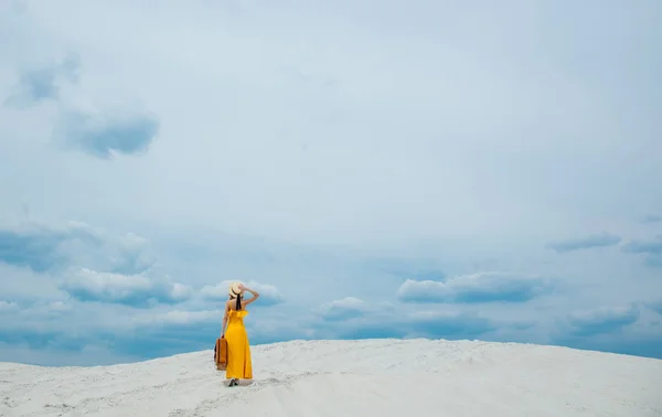 Vrouw in gele jurk met koffer op het strand — Stockfoto