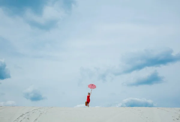 Rotes Kleid mit Regenschirm und Koffer am Strand — Stockfoto