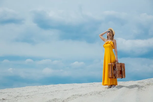 Vrouw in gele jurk met koffer op het strand — Stockfoto