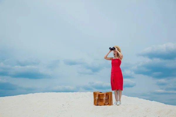 Mujer en vestido rojo con maleta buscando en prismáticos — Foto de Stock