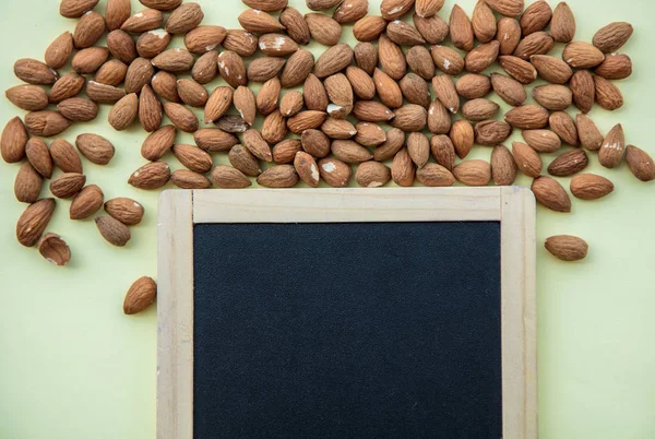 Almonds and blackboard on green background — Stock Photo, Image