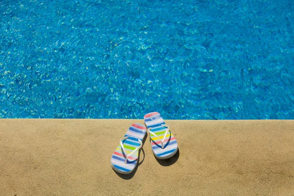 Sandalias de verano de colores cerca de la piscina azul — Foto de Stock