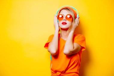 Şık olan kadın turuncu gözlük ve sarı zemin üzerine kulaklıklar. 1980'lerin tarzı kıyafetler