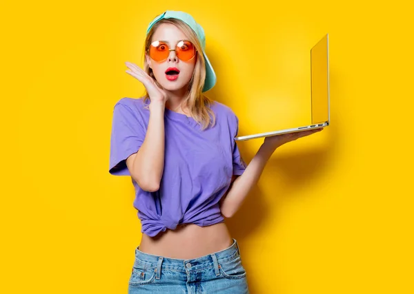 黄色の背景にオレンジ色のメガネとラップトップのコンピューターで若いおしゃれな女性 1980 年代スタイルの服 — ストック写真
