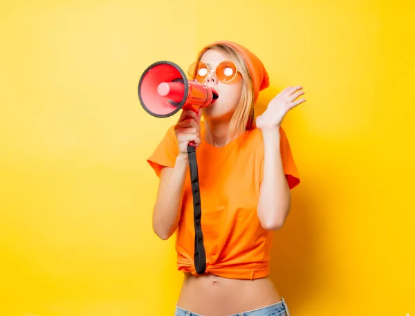 Young style girl in orange clothes with pink megaphone on yellow background. Symbolizes female resistance. Clothes in 1980s style