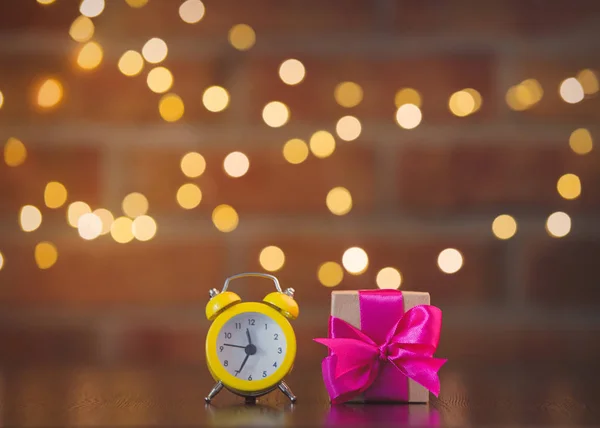 紫弓と背景のボケ味の妖精ライト木製テーブルの上の目覚まし時計と手作りギフト ボックス — ストック写真