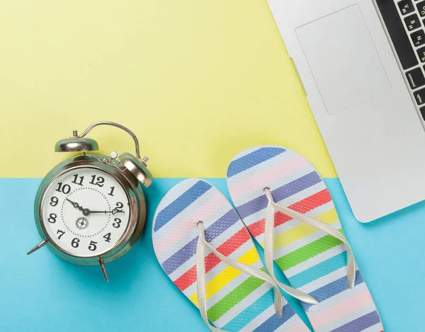 Alarm clock with flip flops near notebook — Stock Photo, Image