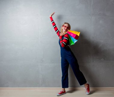 Genç kız kot elbise gri arka plan üzerinde alışveriş torbaları ile stil. 