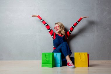 Kot elbise gri arka plan üzerinde alışveriş torbaları ile oturan genç kız stil.