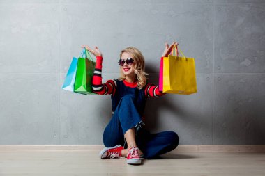 Kot elbise gri arka plan üzerinde alışveriş torbaları ile oturan genç kız stil.