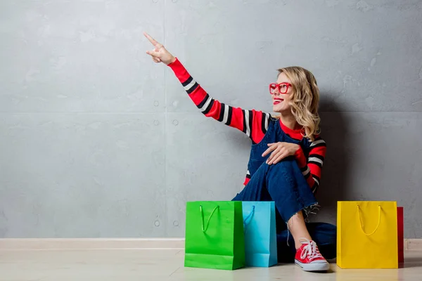 若いスタイルはジーンズ服灰色の背景にショッピング袋で座っている女の子 — ストック写真