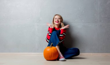 Cadılar Bayramı Balkabağı gri arka plan üzerinde ile katta oturan kırmızı Çizgili kazaklı genç tarzı sarışın kız portresi.