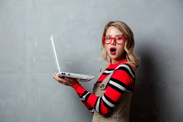 一个年轻时尚的金发女孩的肖像在红色条纹毛衣与笔记本电脑的灰色背景 — 图库照片