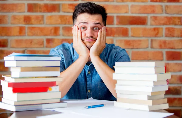 Young tired man with books on a table — Stock Photo, Image