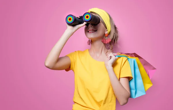 ピンクの背景にカラフルなバッグや双眼鏡を保持している黄色い シャツの若い赤毛の女の子 — ストック写真