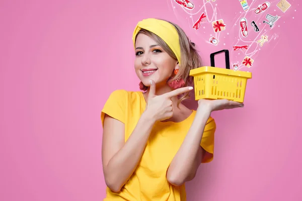 穿着黄色 T恤衫的年轻红发女孩在粉红色背景下持有超级市场篮子 — 图库照片