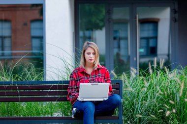 Bankta oturan dışında defter kullanarak çalışan genç kadın.