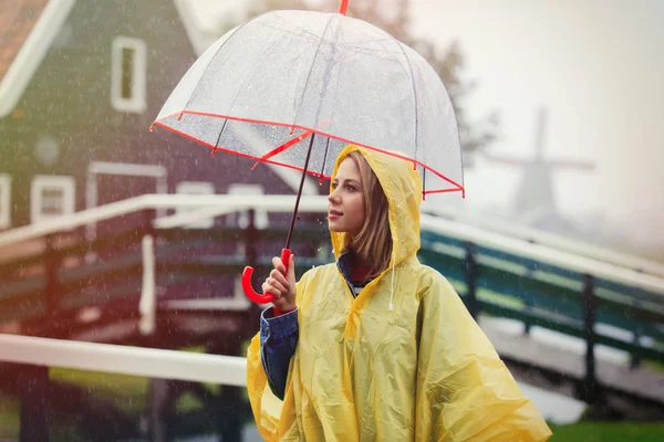 Girl in rain suit with umbrella stay on bridge with dutch house — Stock Photo, Image