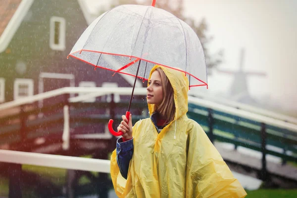 Girl in rain suit with umbrella stay on bridge with dutch mills — Stock Photo, Image