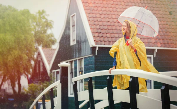 Girl in rain suit with umbrella stay on bridge with dutch house — Stock Photo, Image