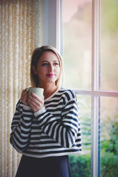 Ung flicka med kopp kaffe bo nära fönster — Stockfoto