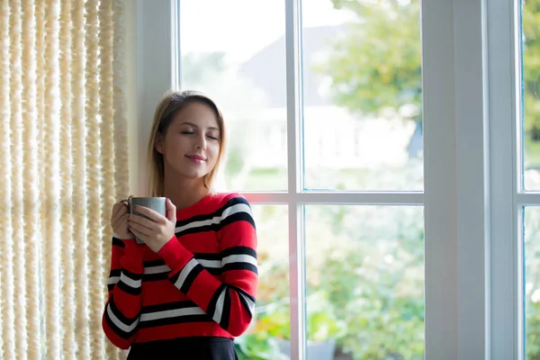 Młoda dziewczyna z filiżanki kawy zatrzymać w pobliżu okna — Zdjęcie stockowe