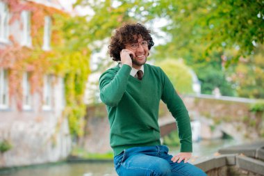 Cep telefonunuzla bir köprü üzerinde oturan genç adam