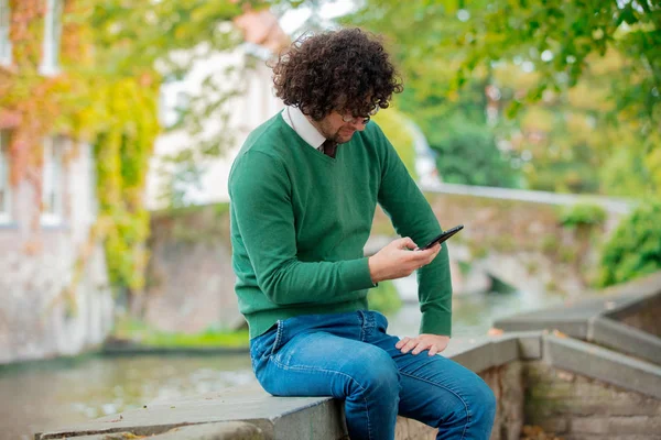 Giovane con cellulare seduto su un ponte — Foto Stock