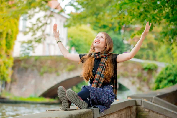 Jovem menina feliz sentado na ponte perto do canal em Bruges — Fotografia de Stock