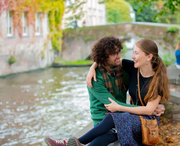 Mladá dívka a muž sedí společně u kanálu v Bruggách — Stock fotografie