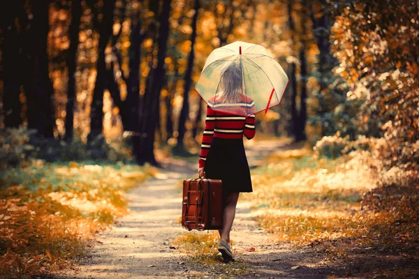 Девушка с зонтиком и чемоданом в осеннем парке — стоковое фото