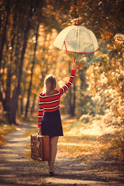 Девушка с зонтиком и чемоданом в осеннем парке — стоковое фото
