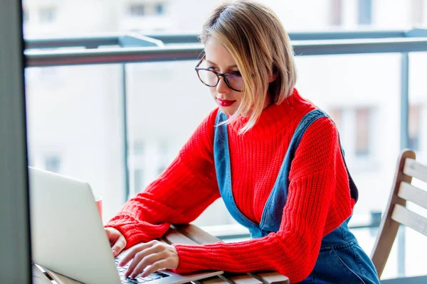Ragazza in maglione rosso seduta a tavola con computer — Foto Stock