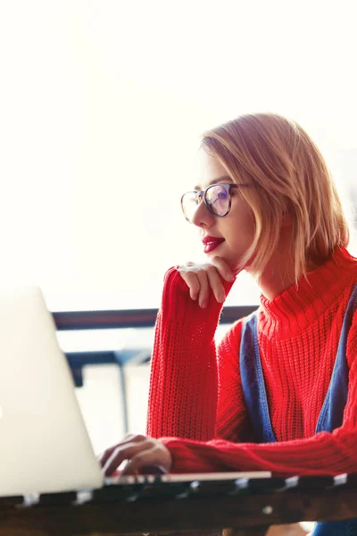 Ragazza in maglione rosso seduta a tavola con computer — Foto Stock