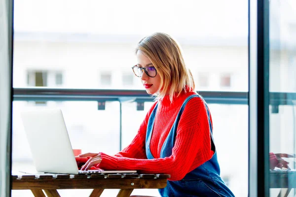 Dziewczyna w czerwonym swetrze siedzi przy stole z komputera — Zdjęcie stockowe