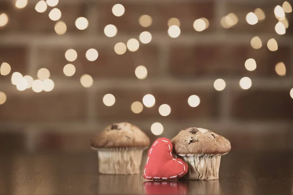 Real homemade classic cupcakes and heart shape toy. Fairy lights and gift box in bokeh background. Christmas time concept