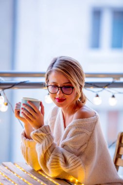 Saat akşam çevre peri ışıkları masada oturmuş kahve olan kadın.