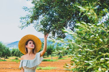 Elbise ve şapka giyen genç kızıl kız Yunanistan 'ın Girit kentindeki Yunan zeytin bahçesinde dinleniyor