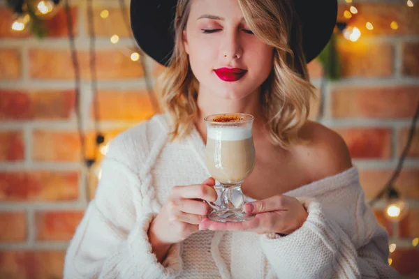 一个年轻的穿着白色毛衣的女人的肖像与杯咖啡 圣诞灯和松树分行 — 图库照片