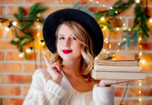 本とクリスマスの照明と背景に松の枝に白いセーターで居心地の良い若い女性の肖像画 — ストック写真