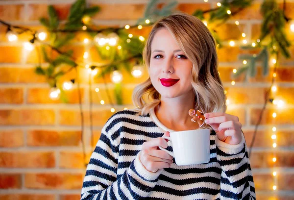 一杯のコーヒー クッキー クリスマス ライト 松の枝の白いセーターで居心地の良い若い女性の肖像画 — ストック写真