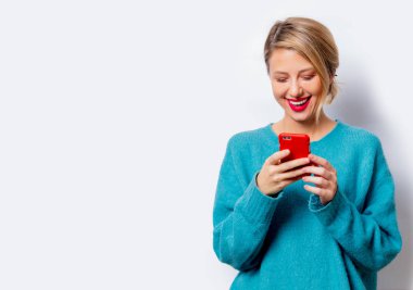 Mavi kazaklı izole beyaz arka plan üstünde hareket eden telefon ile güzel bir beyaz gülümseyen kadın portresi.