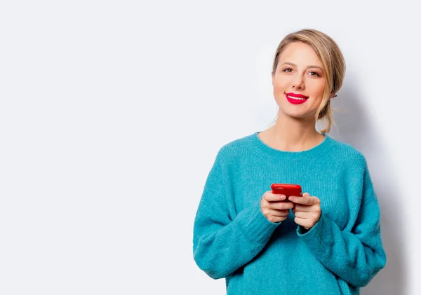 白い背景の分離上の携帯電話に青いセーターの美しい白い笑顔の女性の肖像画 — ストック写真