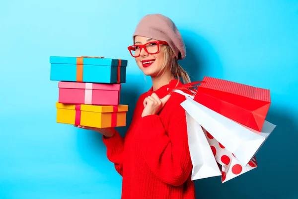 一个年轻女孩的肖像在红色毛衣与礼品盒和购物袋的蓝色背景 — 图库照片